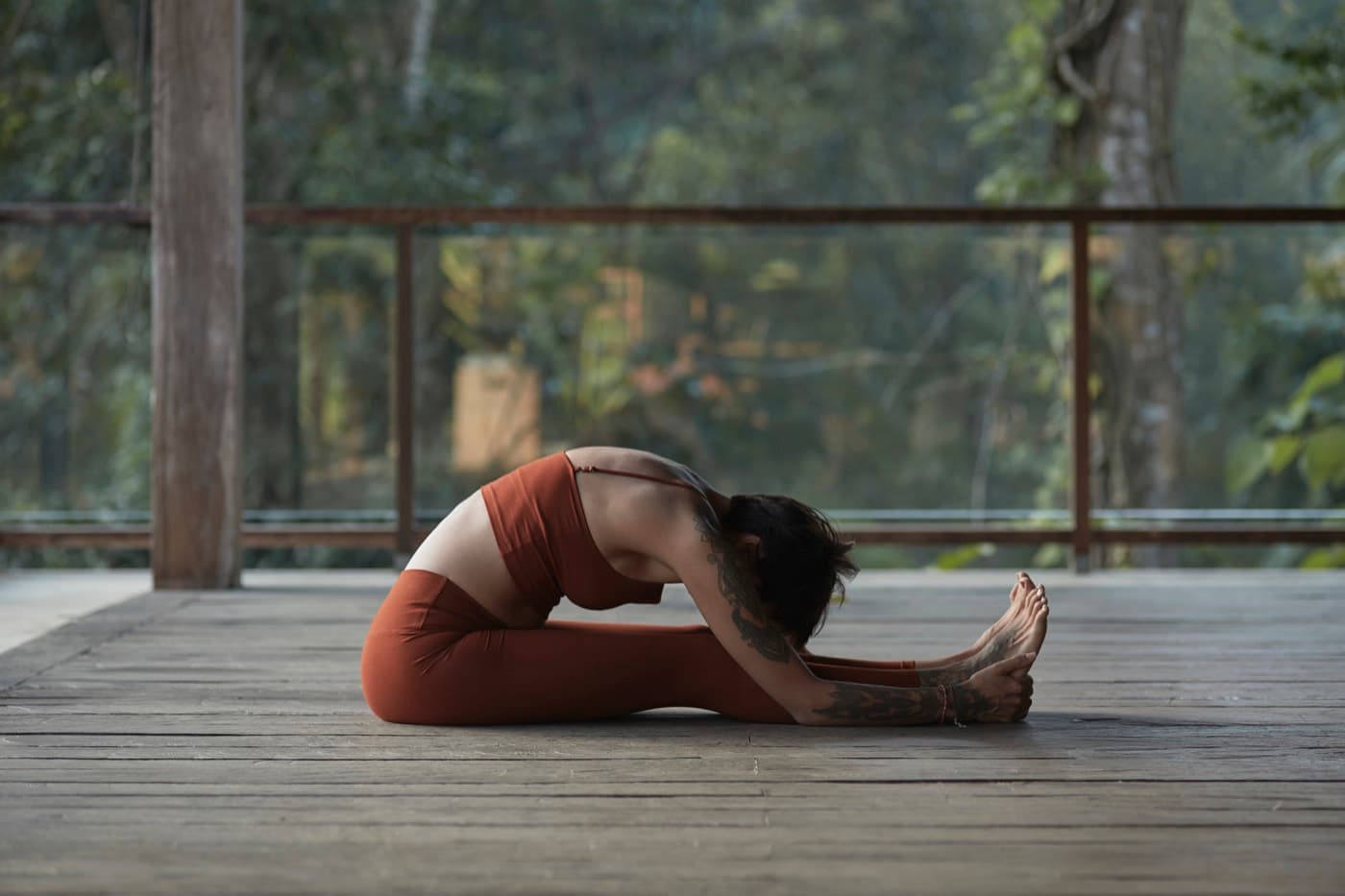 A student in a seated forward fold on a jungle deck.
